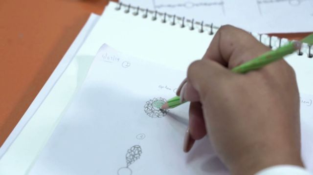 A designer's hand sketching and colour-shading a gemstone setting on a design pad (poster frame)